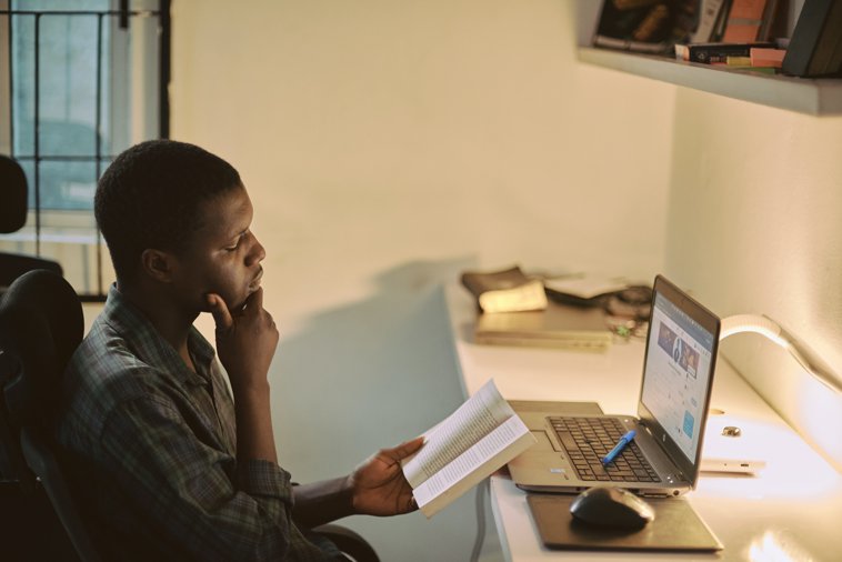 man reading book at laptop