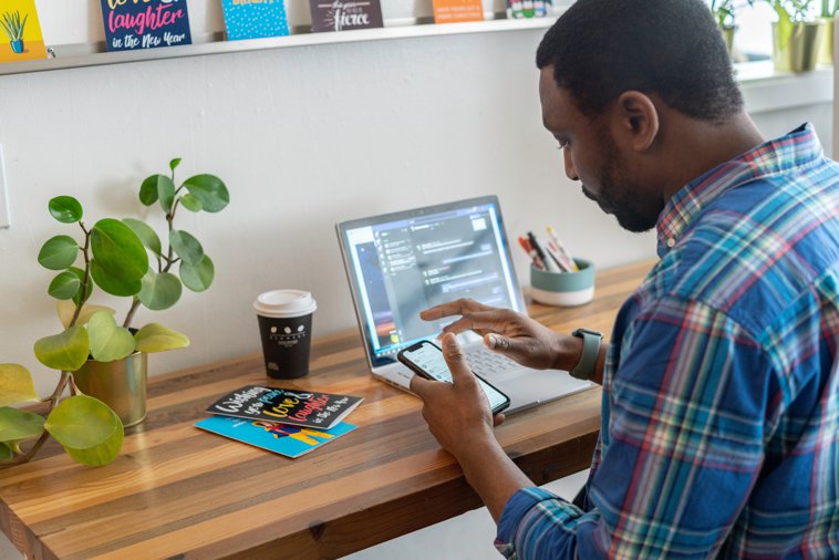 man working on phone with laptop